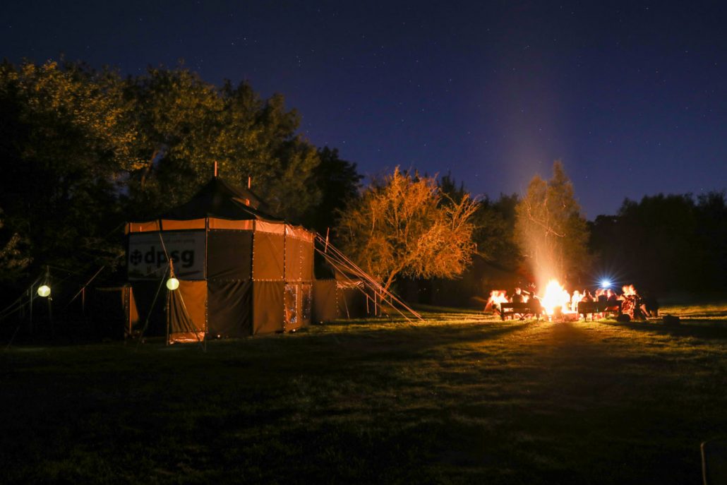 Zeltplatz auf dem ein großes Zelt steht mit Lagerfeuer am Abend